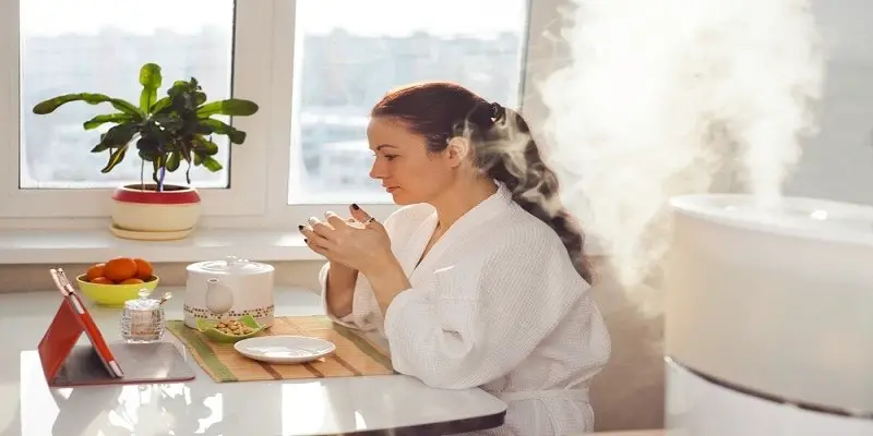 Woman drinking tea reading tablet at an ultrasonic humidifier