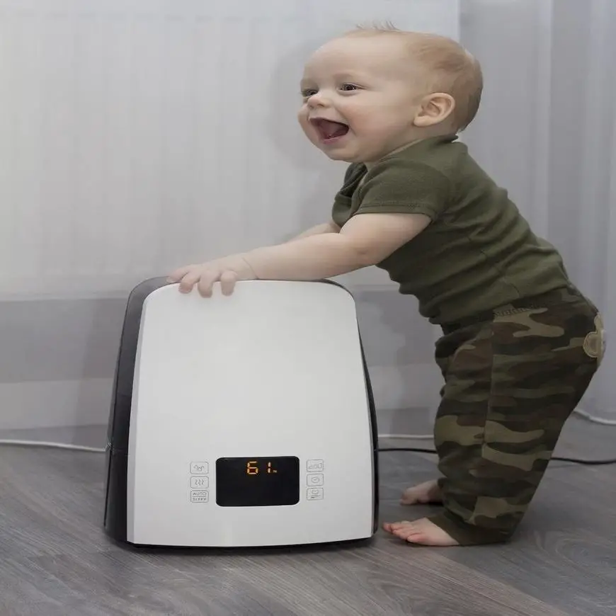 An infant kid staying leaning against the humidifier. Laughing and smiling lovely toddler.