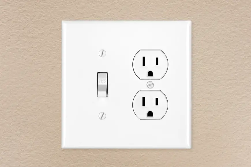A brand new modern electrical toggle light switch and power outlet on a freshly painted wall.