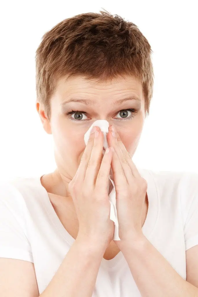Woman in short hair blowing her nose on the tissue on white background