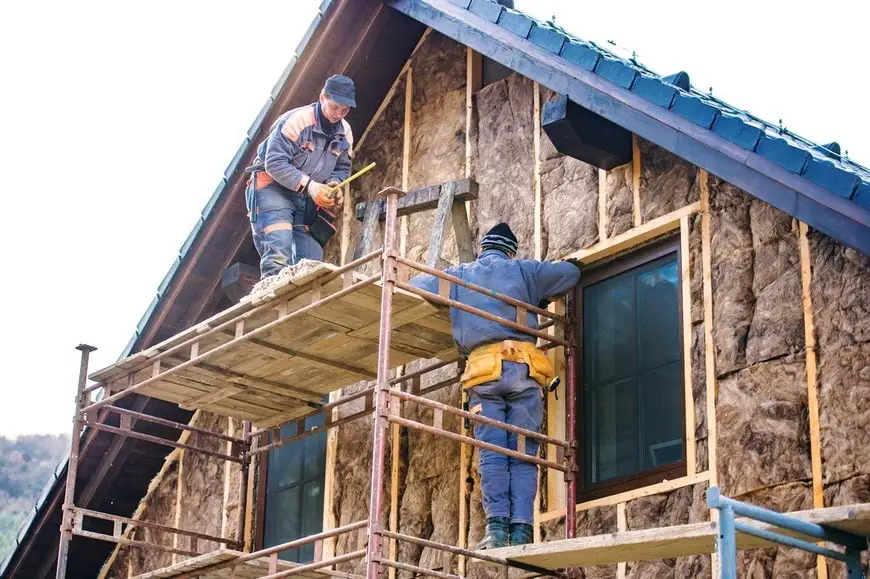 Construction workers thermally insulating house facade with glass wool.
