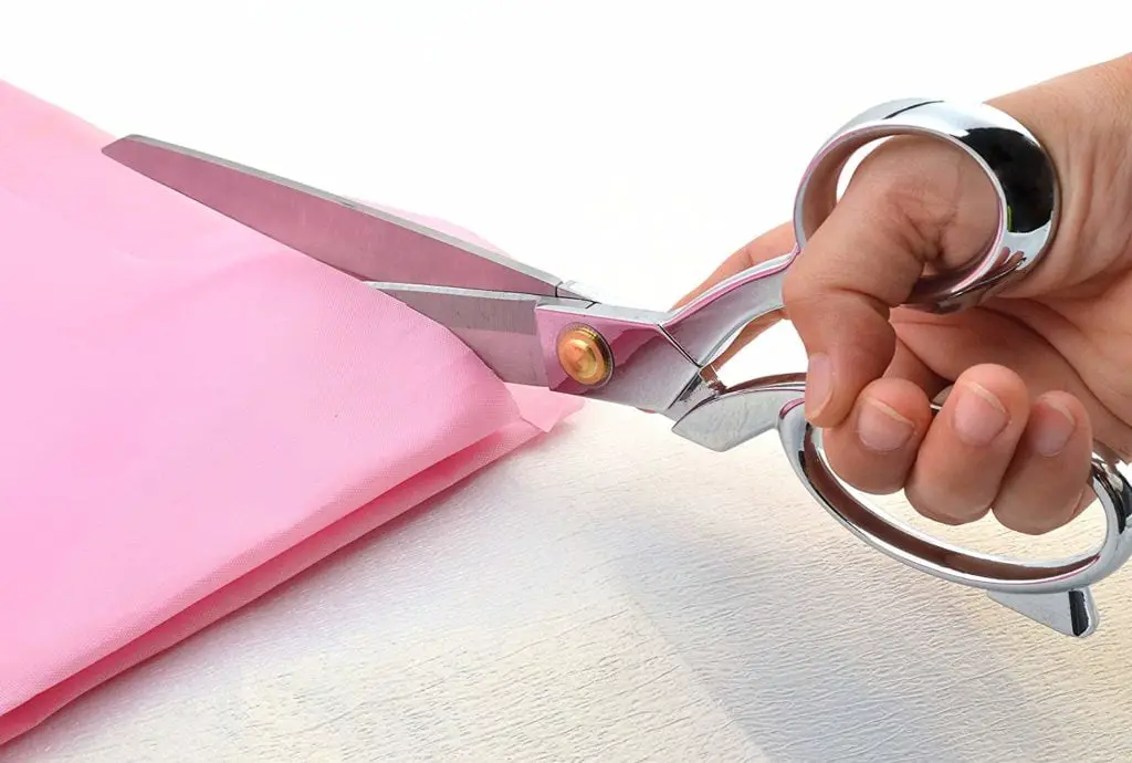 Cutting a pink fabric using a scissors