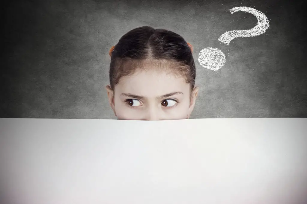 Closeup portrait little girl, suspicious, scared, cautious, curious, hiding behind blank white paper billboard, blank sign, space for text looking side way isolated black background with question mark