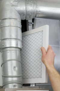 A man's arm and hand seen replacing disposable air filter in home central air furnace.
