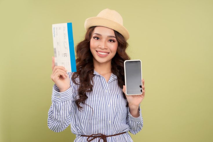 Image of successful voyage girl 20s expressing delight while holding air tickets and smartphone in hands isolated over green background