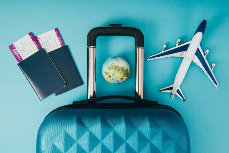 Top view of globe and plane models, travel bag and passports with tickets on blue background